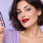 Portrait beauté avec une bouche rouge, des cils nus et un tube de mascara fermé.