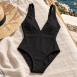 Maillot une pièce noir à décolleté en V posé sur du lin près du chapeau.