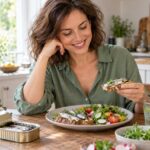 Une femme adulte apprécie un repas de sardines et de légumes dans sa cuisine.