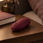 Petit accessoire intime bordeaux à forme arrondie sur une table de chevet.